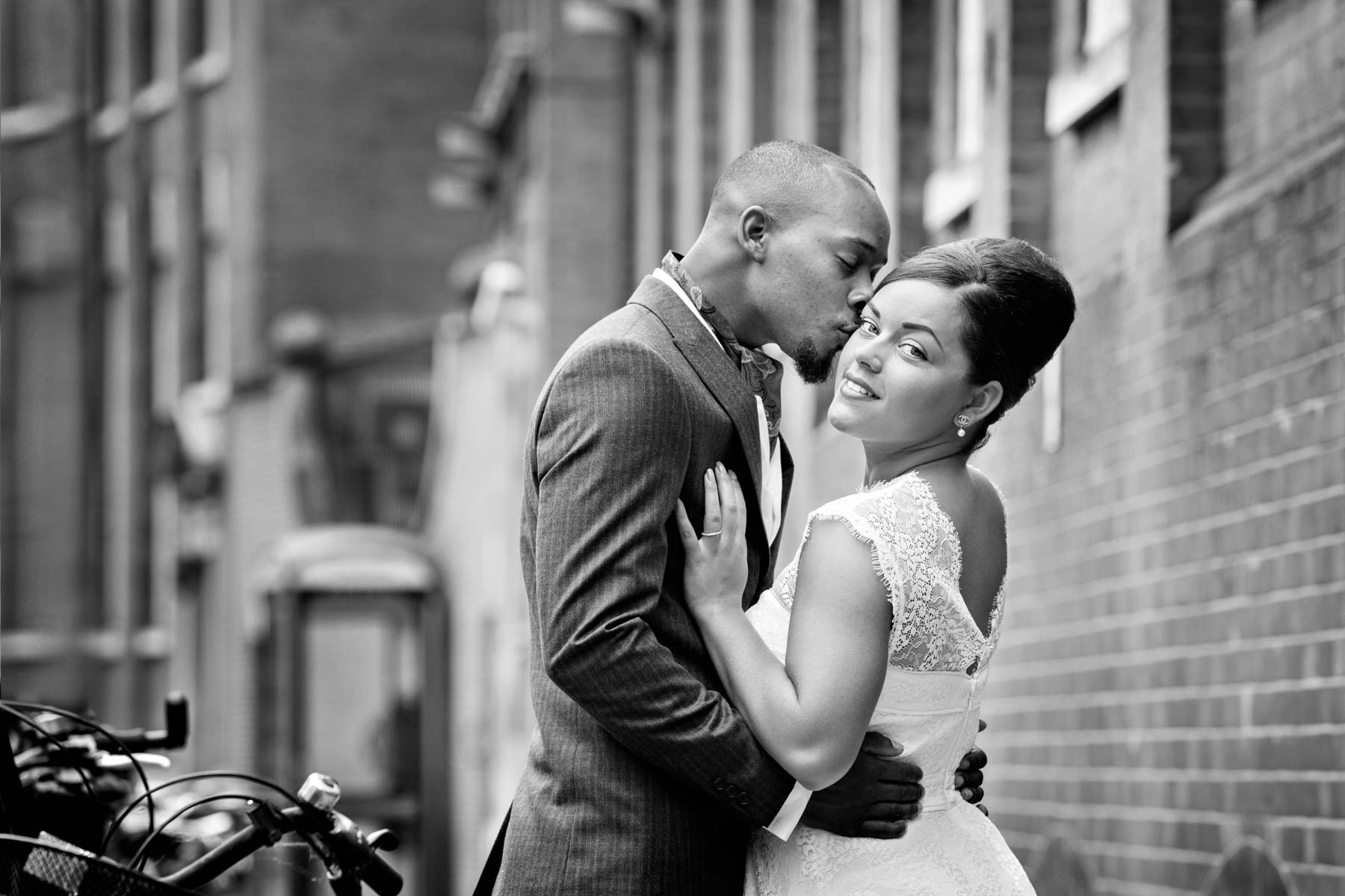 A sensual black and white wedding portrait in Chelsea with the bride smiling sexily at the camera whilst the groom kisses her on the cheek.