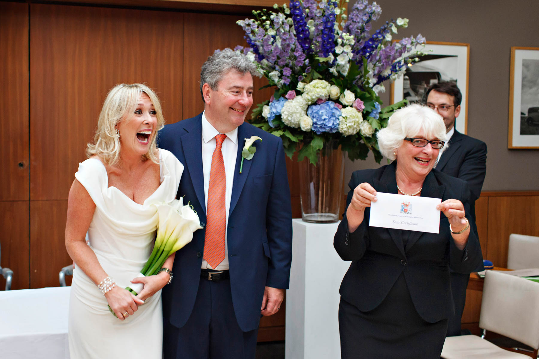 A cheerful bride and groom receive their wedding certificate from the Chelsea and Kensington registrar, at their Bluebird Chelsea wedding ceremony.