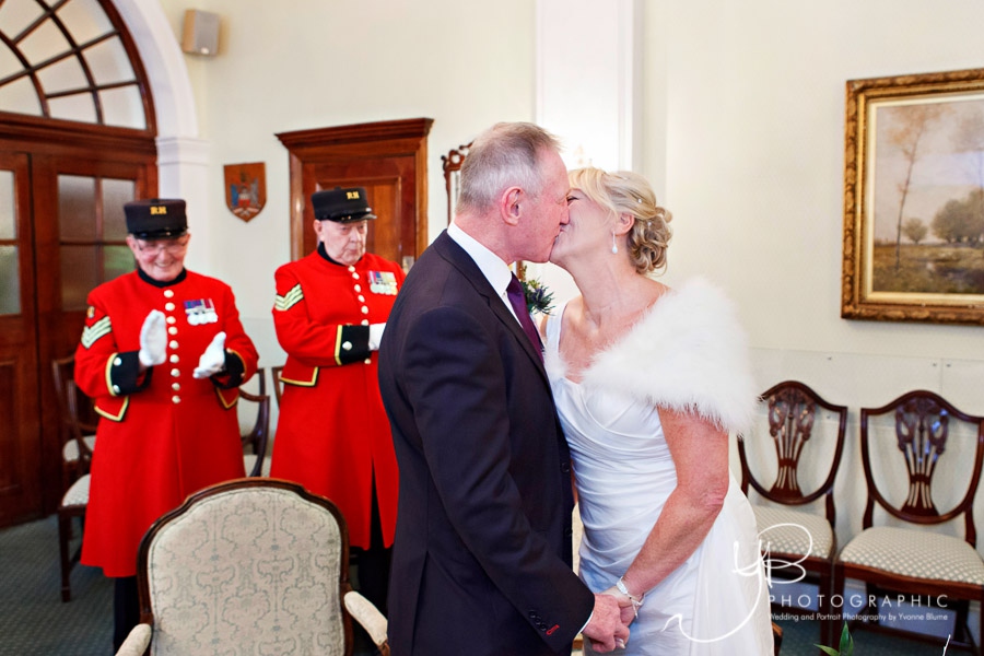 A bride and groom kiss after their Christmas elopement and intimate ceremony in front of two Chelsea Pensioners. 