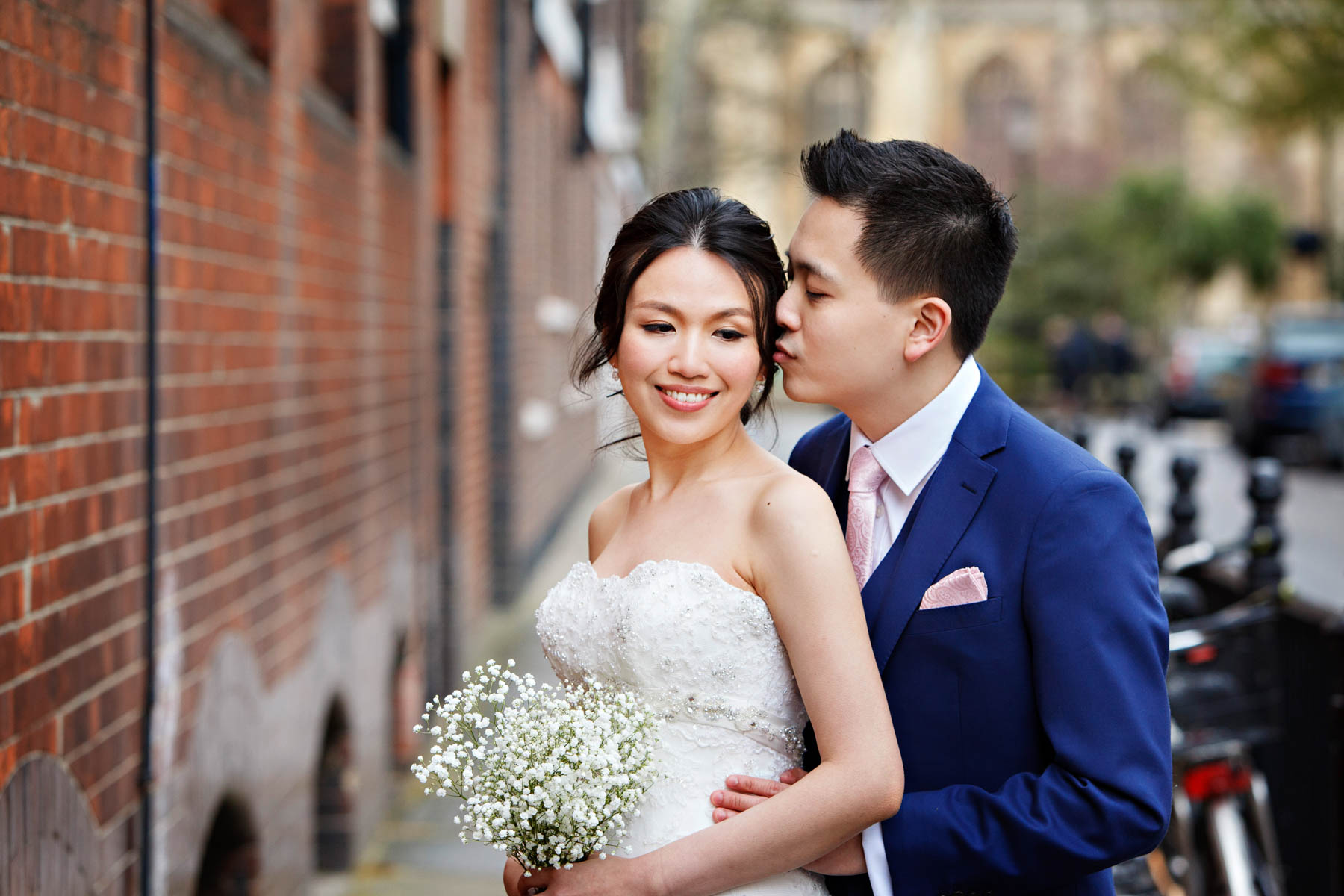 A Chinese bride and groom cuddle together for a romantic wedding portrait in Chelsea after their Chelsea Old Town Hall Wedding. The groom is kissing the bride on the cheek.