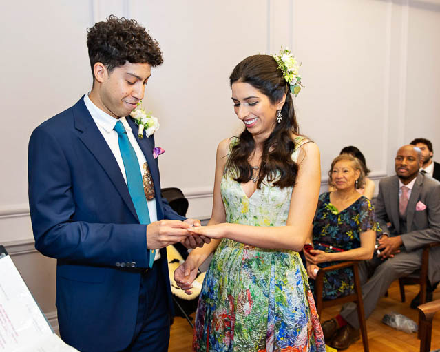A bride in a colourful dress exchanges vows with her groom in a navy suit in the Knightsbridge Room in London's Westminster City.