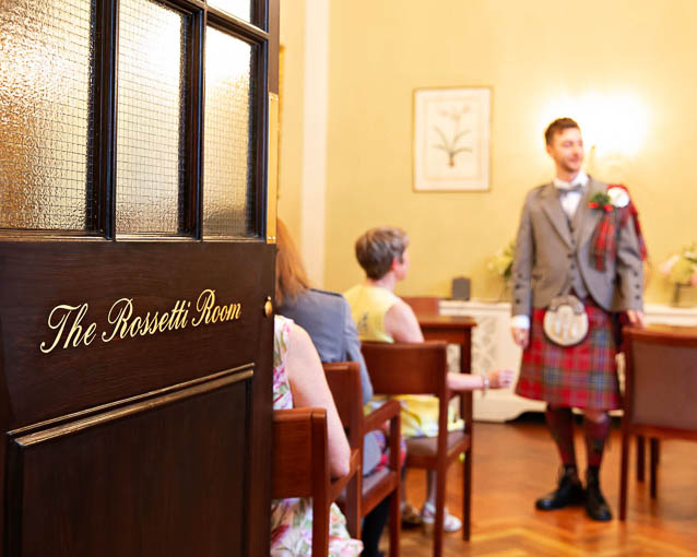 The Rossetti Room door opens onto groom in a red tartan kilt before his civiil wedding ceremony in Kensington and Chelsea Register Office.