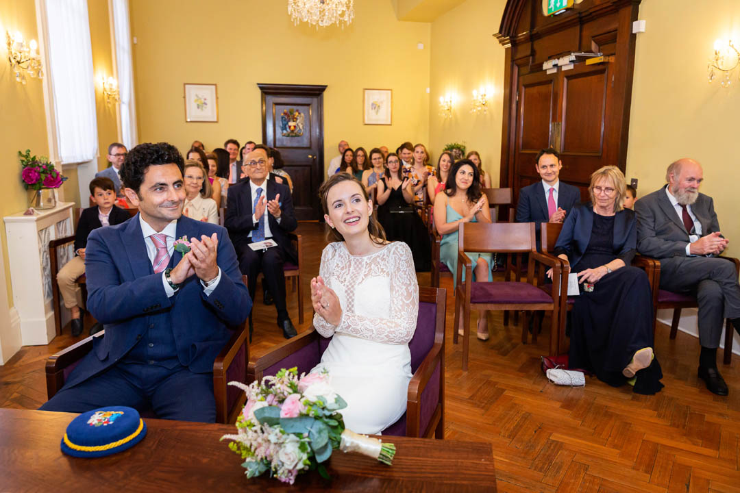 The wedding couple and their guests applaud the bridesmaid who has just delivered a reading.