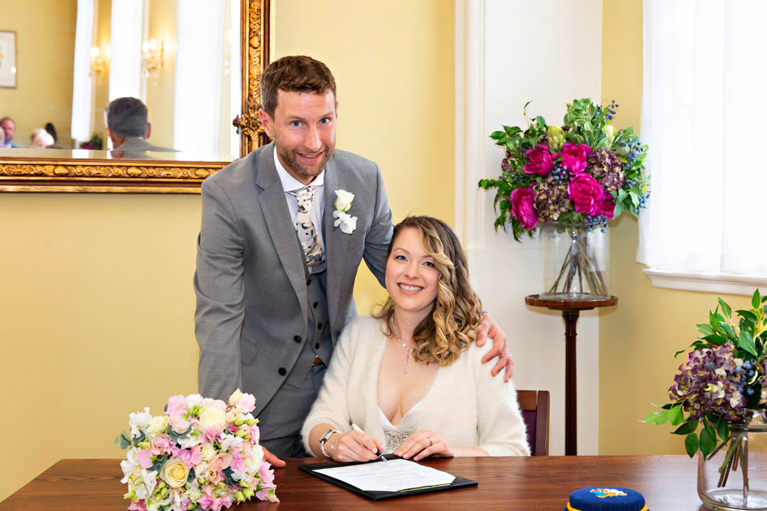 A bride and groom pose for a formal photograph after signing their wedding schedule in the Brydon Room