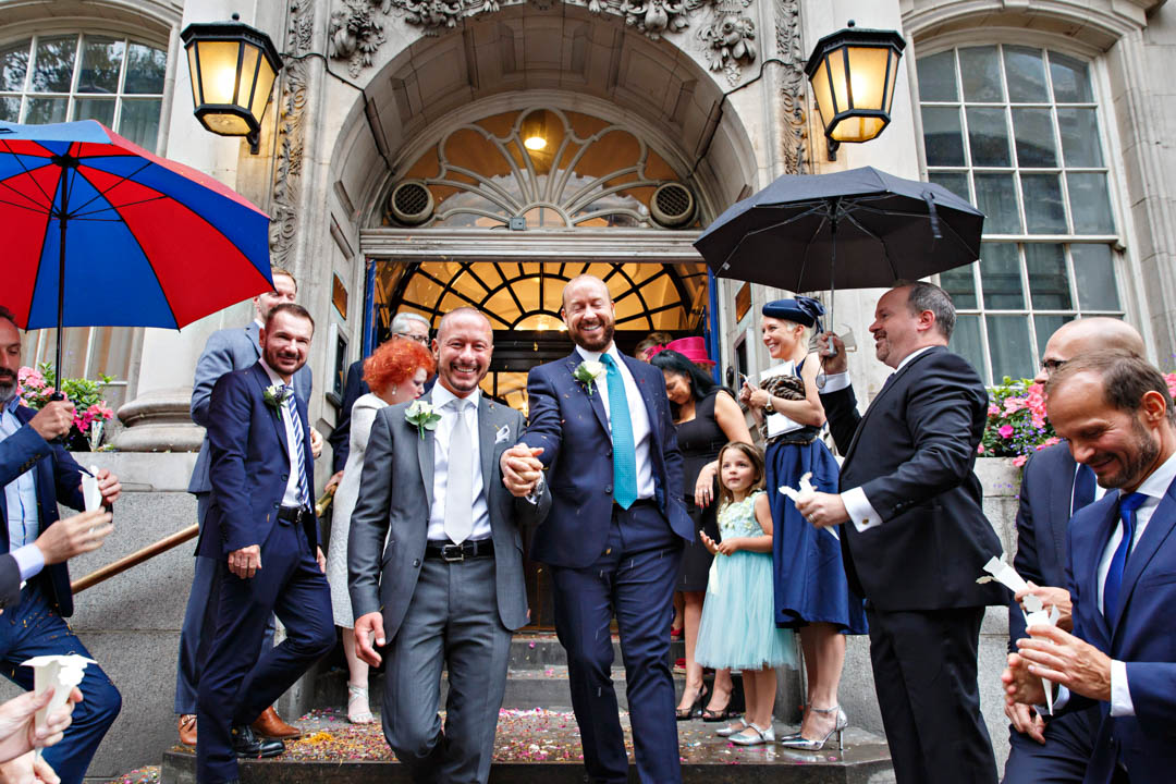 Two grooms exit Chelsea Town Hall on a rainy day, after they Brydon room civil wedding.