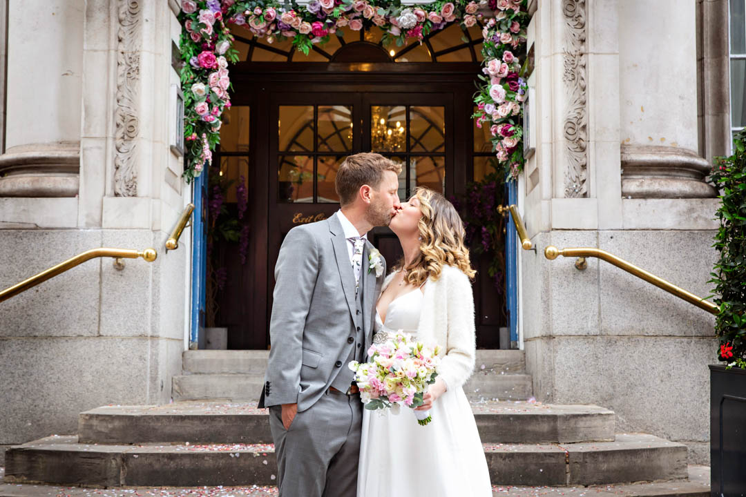 A bride and groom kiss on the steps of Chelsea Old Town Hall