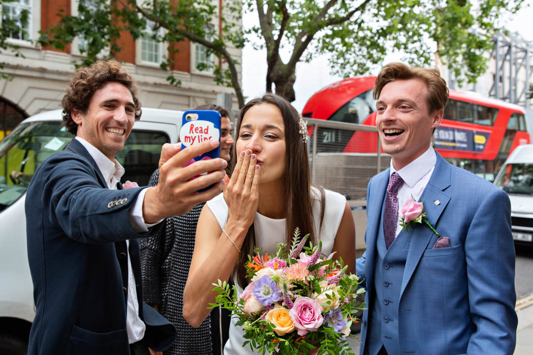 A bride and groom blow kisses to their family on zoom on the King's Road after their Brydon Room wedding.