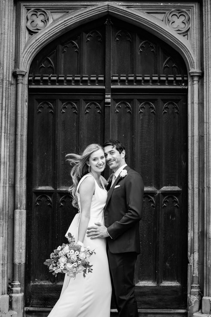 Moody black and white wedding portrait of a bride and groom posing in front of distressed church door in Chelsea.