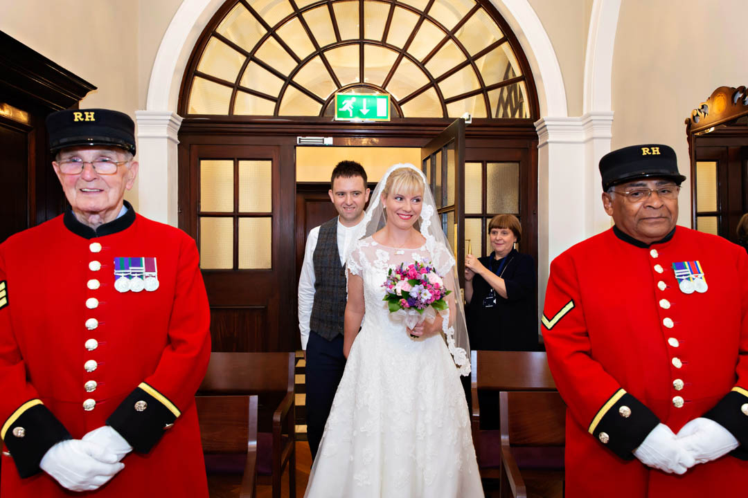 The bride and groom walk down the aisle amongst their Chelsea Pensioner witnesses in the Harrington Room