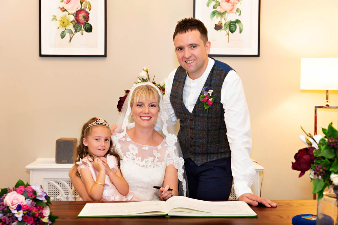 Bride and groom pose with their little girl and the wedding register during their civil ceremony at Chelsea Old Town Hall