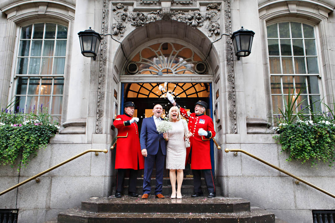Chelsea Pensioners in red tunics throw confetti over bride and groom on the steps of Chelsea Town Hall.