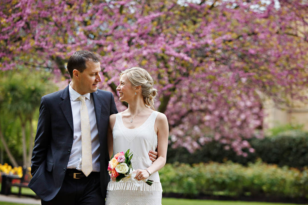 Bride and groom walk in the park in Chelsea for their wedding portraits with cherry blossoms in the background.