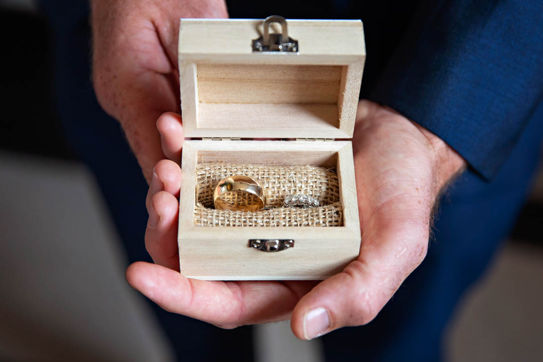 The best man holds open a wooden box containing the two wedding rings set into hessian.
