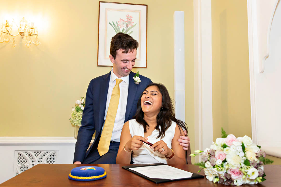Two newlyweds laugh together while signing paperwork during their civili marriage in the Rossetti Room.