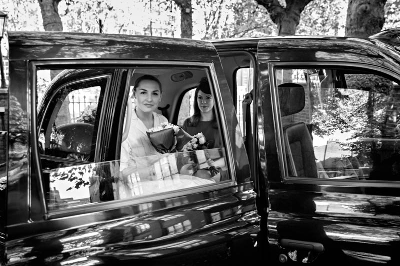 Black and white photograph of a bride through a black London taxi window, as she arrives at Southwark register office to get married.