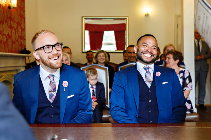 Two grooms in matching royal blue suits beam with joy at the start of their civil wedding at Southwark register office.