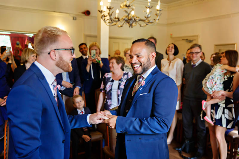 A groom can't hide the joy from his face as he place the ring on the second groom's hand in this same sex civil wedding at Southwark.