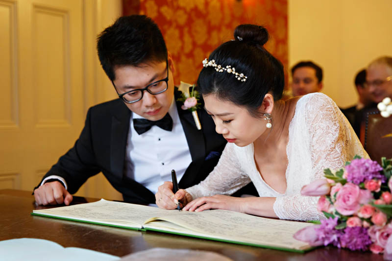The bride and groom are in deep concentration as the bride signs the wedding register during their intimate winter wedding at Southwark Register Office.