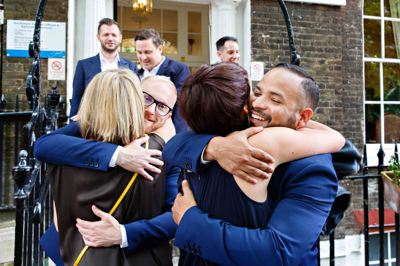 Two grooms joyously hug their guests as they exit their Southwark civil wedding.
