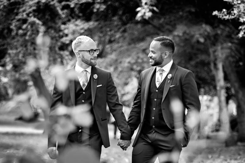 A black and white photograph of two grooms strolling through the park holding hands, after their wedding at Southwark Register Office.