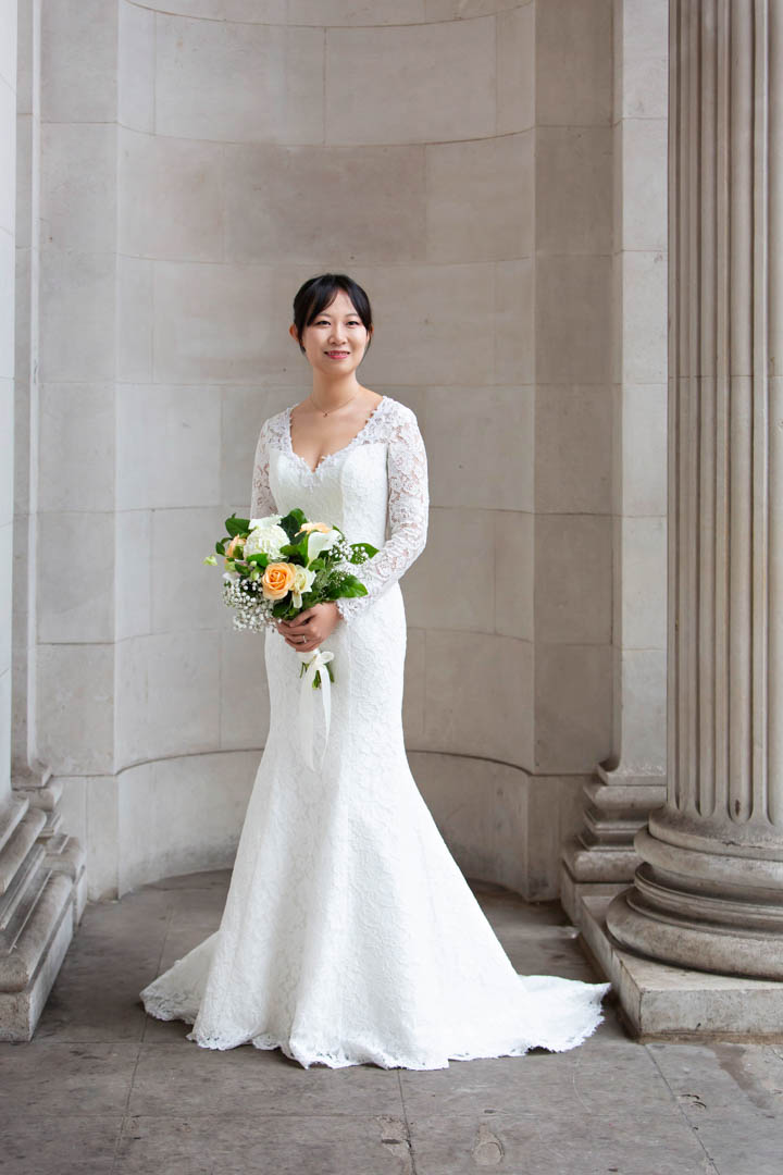 A Chinese bride in an elegant full-length white lace gown poses for her bridal portrait at The Old Marylebone Town Hall