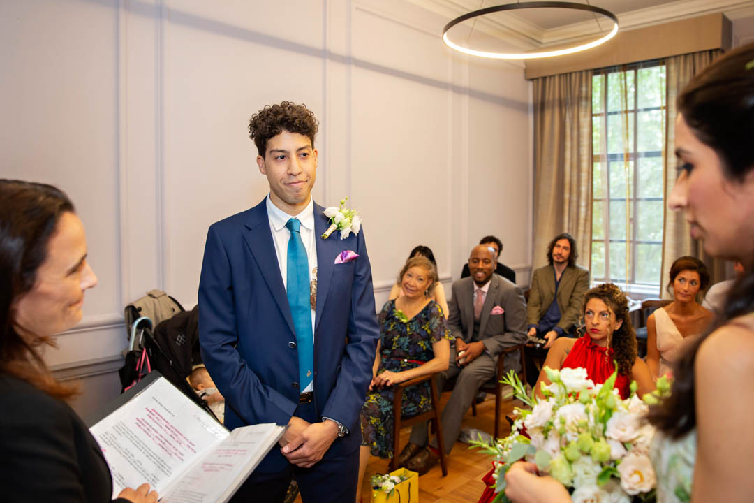 A groom looks at his bride with pride as she confirms her name for the registrar during their Knightsbridge wedding.