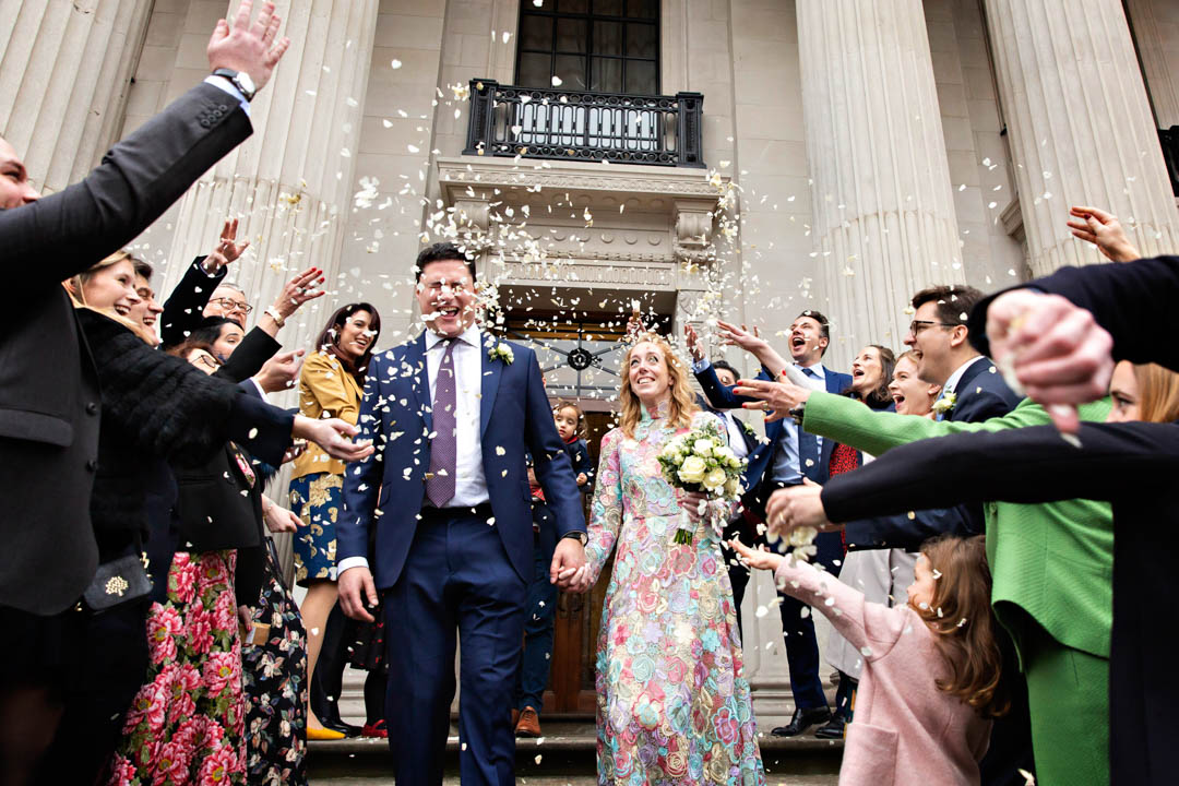 Bride and groom walk into a flurry of confetti thrown by their guests at the iconic Old Marylebone Town Hall