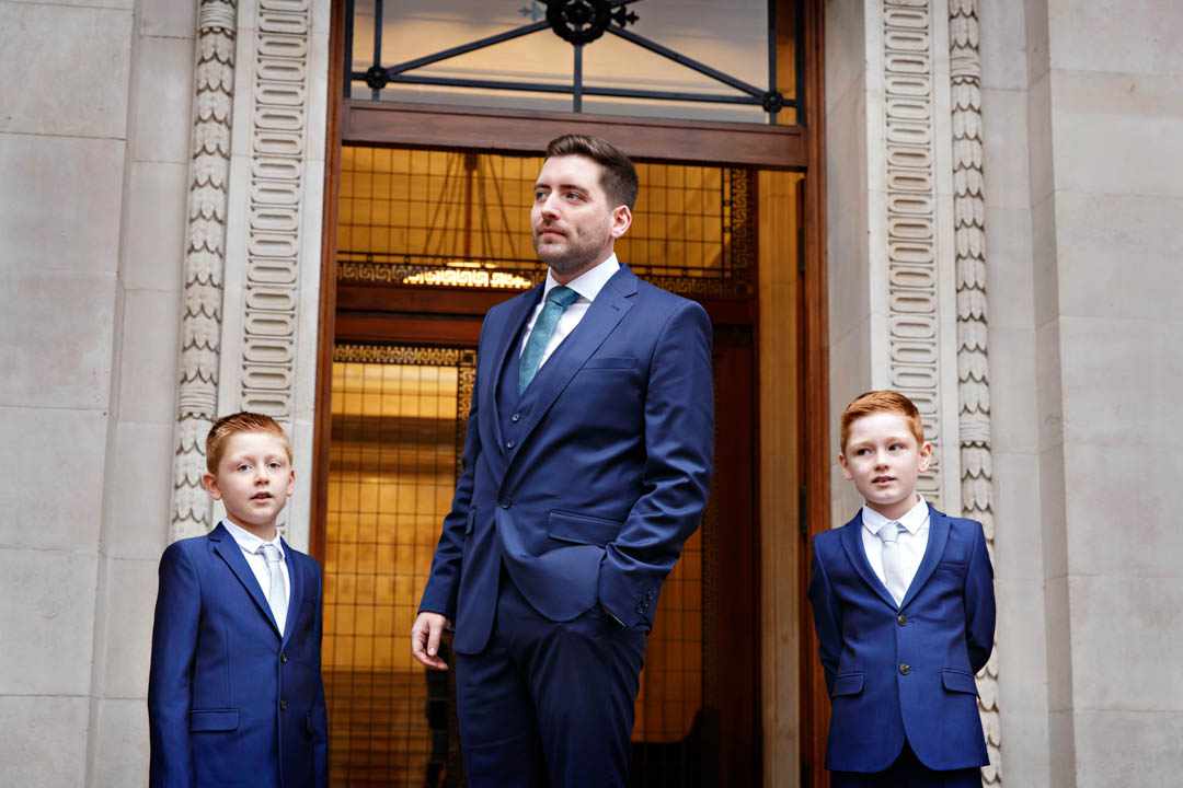 The groom looks into the distance waiting for his bride to arrive. His two little paige-boys wait with him.