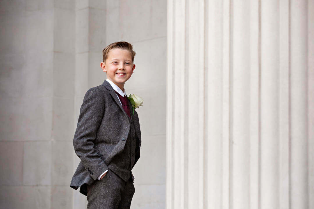 A young groomsman looks delighted to have a special role in today's register office wedding in the Marylebone room.