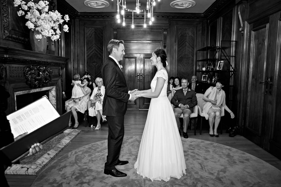 A black and white, wide-angled photograph of the Marylebone as the bride and groom exchange wedding vows.