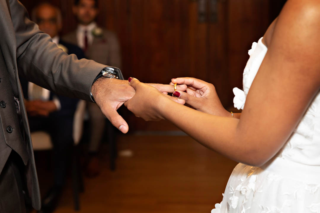 A close-up image of the bride placing the wedding ring on the groom's finger.