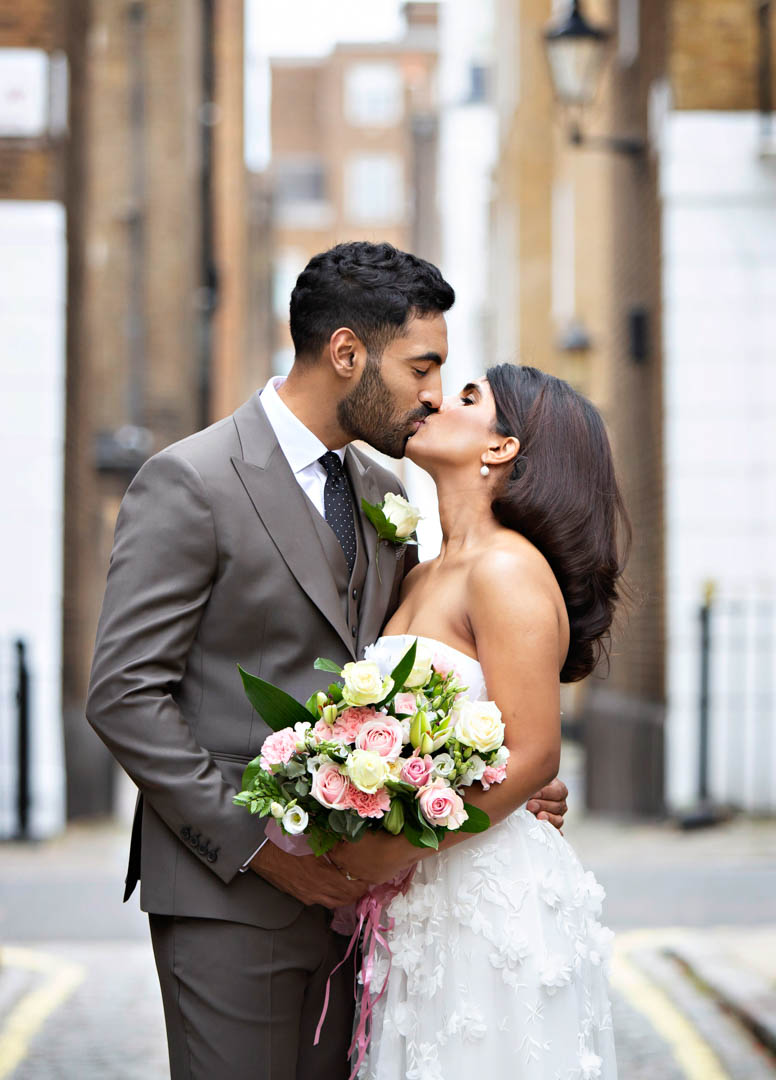 A bride and groom share a kiss during their wedding portraits in a cobbled mews in Marylebone.
