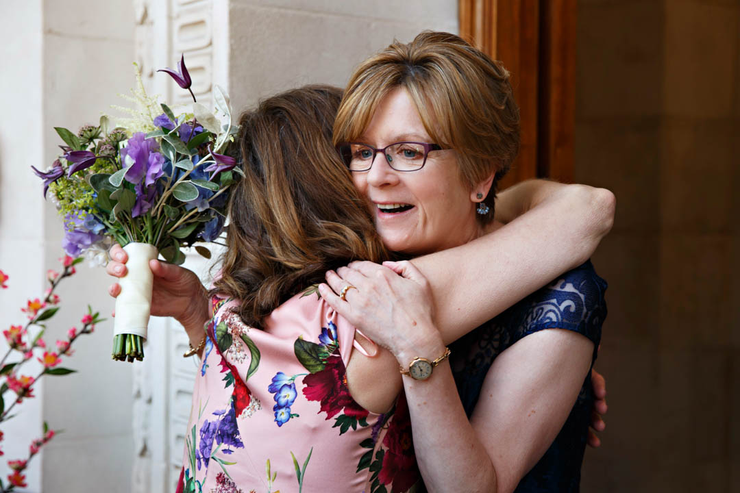 A bride hugs a guest who has just arrived at The Old Marylebone Town Hall. The bride will be getting married in the Mayfair Room.