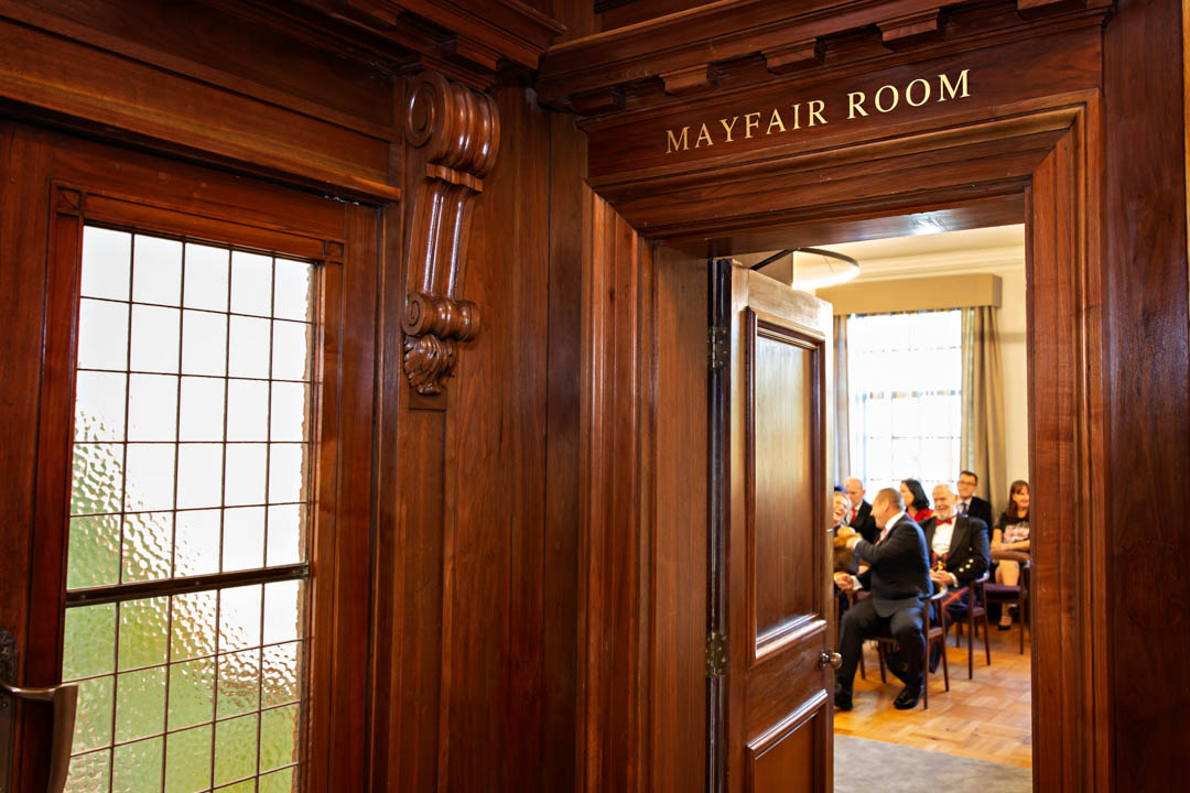 This photo shows a peek into the Mayfair Room from the wood-panelled hallway. Through the doorframe you can see that guests are assembled and seated, ready for the wedding ceremony to begin.