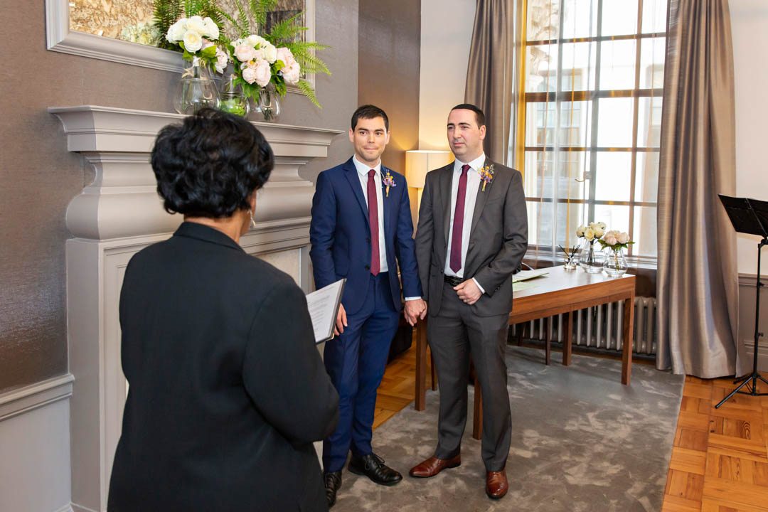 Two grooms look serious as they pay close attention to the registrar during their gay civil partnership ceremony in the Mayfair Room.
