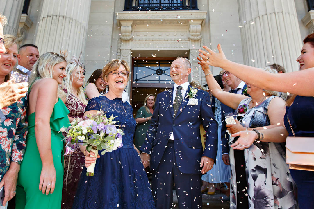 A mature bride and groom exit the Old Marylebone Town Hall into a big confetti throw on the stone steps.