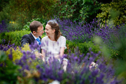 Bride and groom cuddle up for a romantic wedding portrait, sitting among bluebells at Morden Park House.