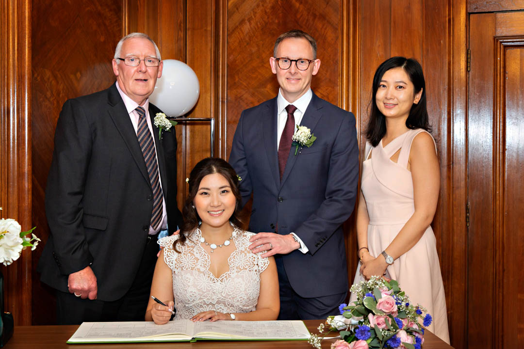 A bride and groom pose for a formal photograph, with their wedding witnesses after signing the wedding register in the Paddington Room.
