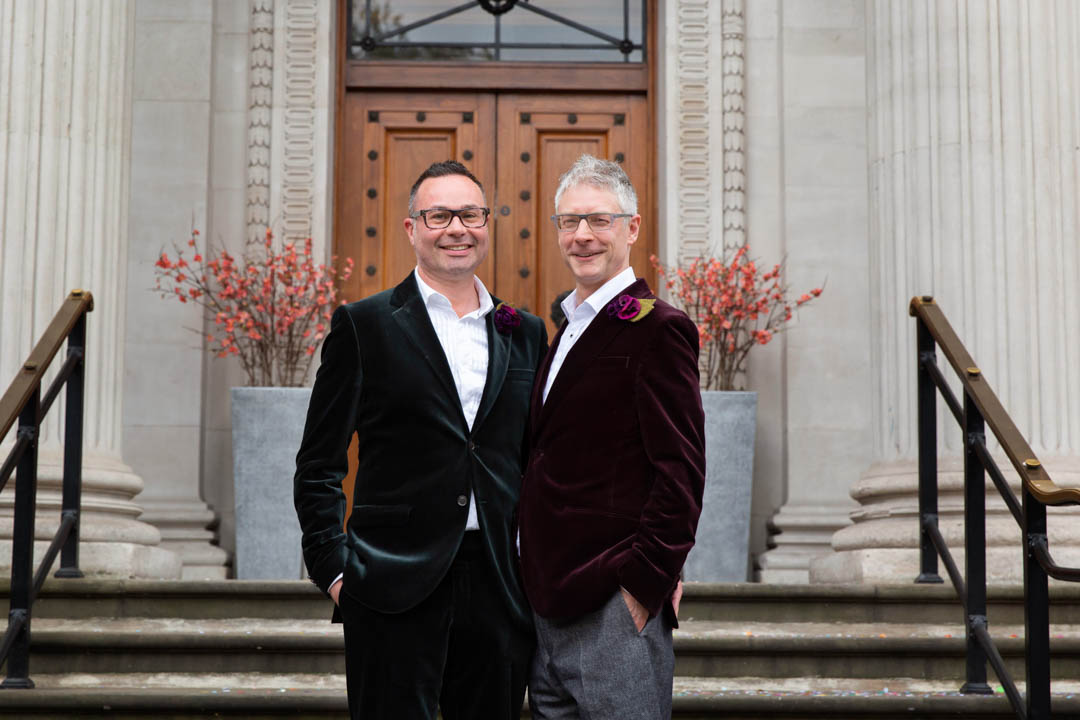 Two grooms pose for their wedding portraits on the steps of Old Marylebone Town Hall, after their same sex civil ceremony in the Paddington Room.