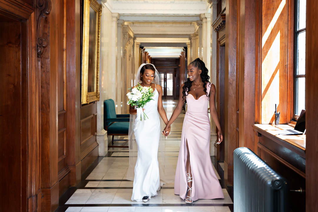 A bride and her daughter walk down a hallway on the way to the Pimlico Room for her wedding.