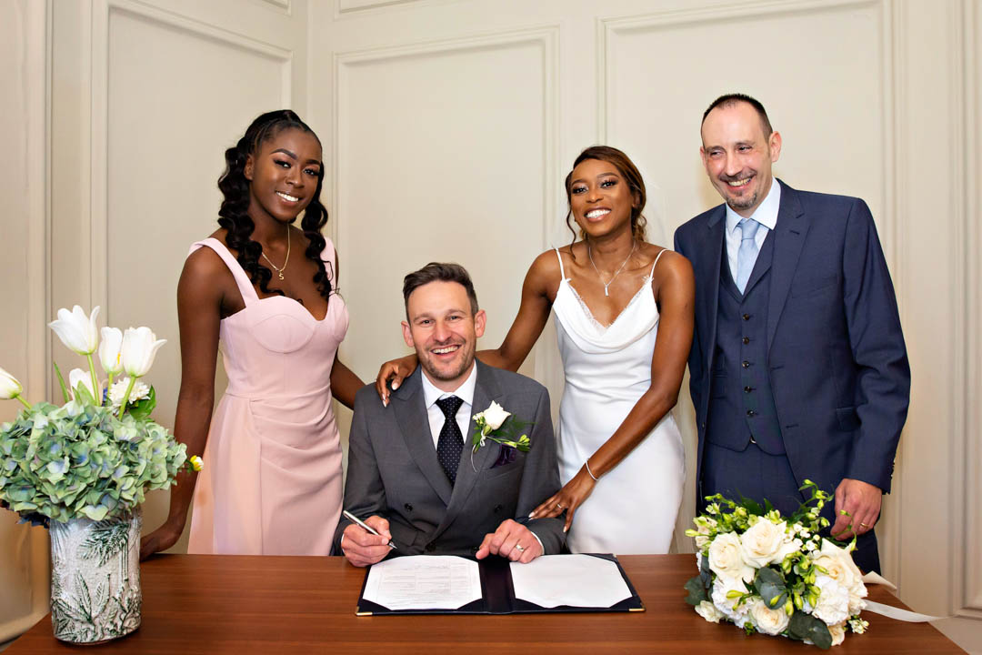 A groom with his bride and their two witnesses take care of paperwork during a civil marriage ceremony in the Pimlico Room.