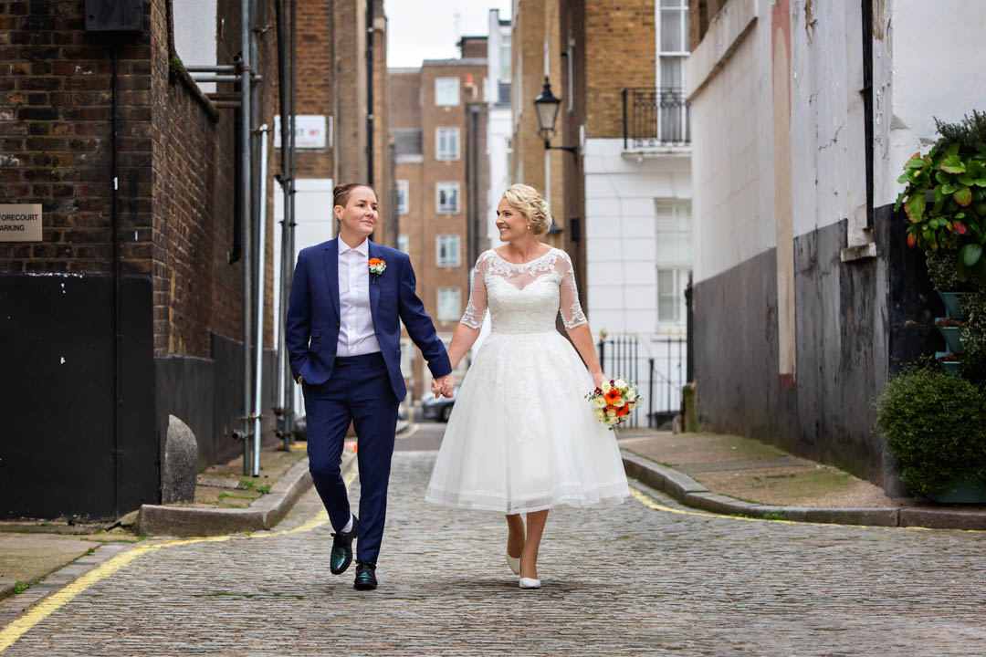 Two newlyweds walk down a cobbled lane in London's Marylebone after marrying in the Pimlico Room at Westminster City Council's Old Marylebone Town Hall.