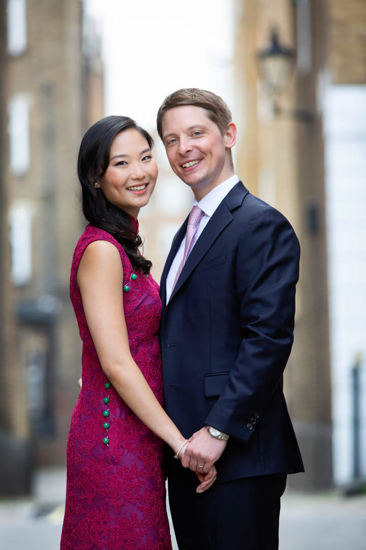 A bride wearing a cerise cheongsam with green buttons poses with her groom in a Marylebone street, after marrying in the Pimlico Room at Old Marylebone Town Hall.