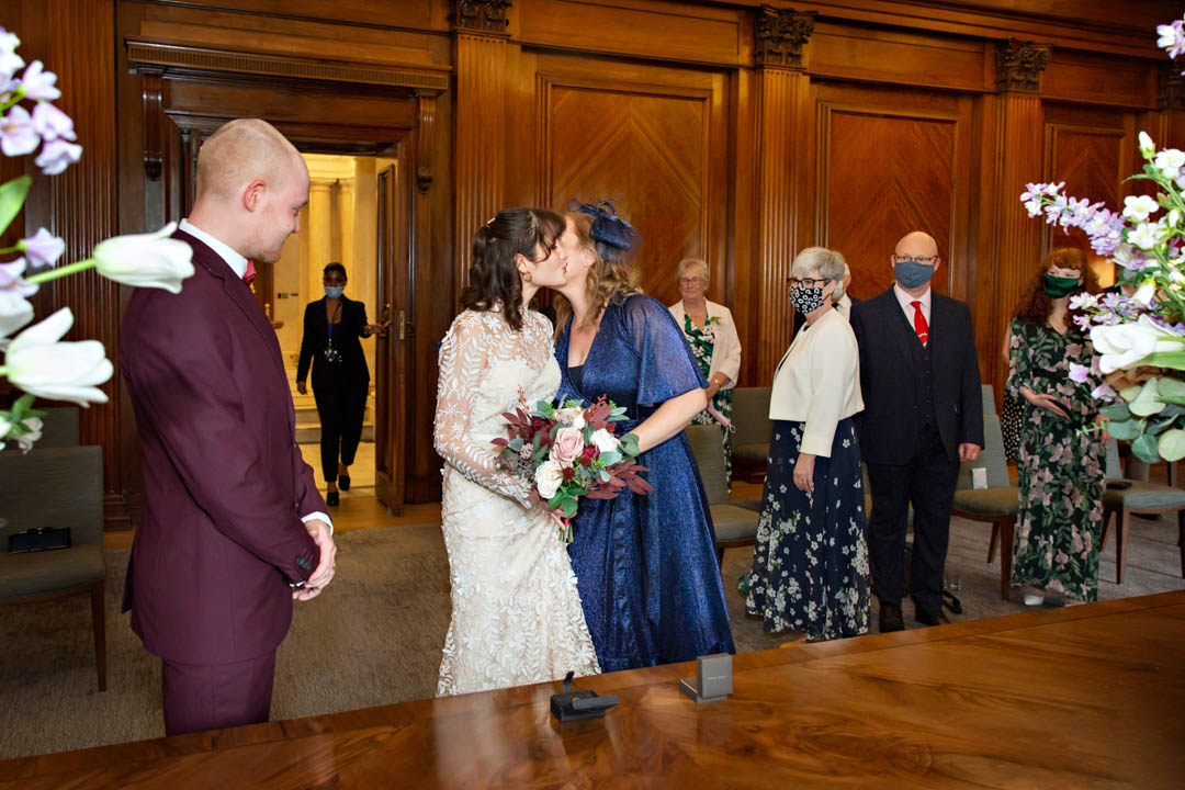 The bride's mother kisses her daughter on the cheek after walking her down the aisle into her Westminster room wedding.