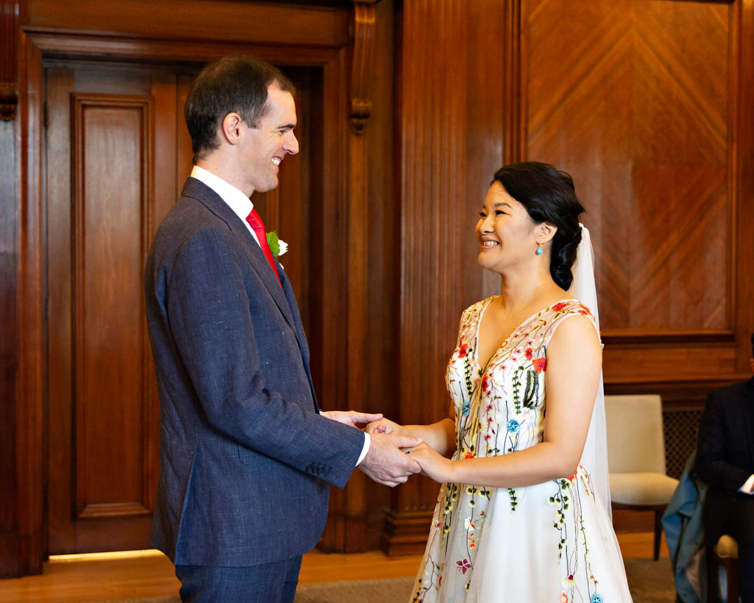 A bride and groom beam big smiles at each other as they exchange wedding vows during their intimate register office wedding in the Westminster Room.