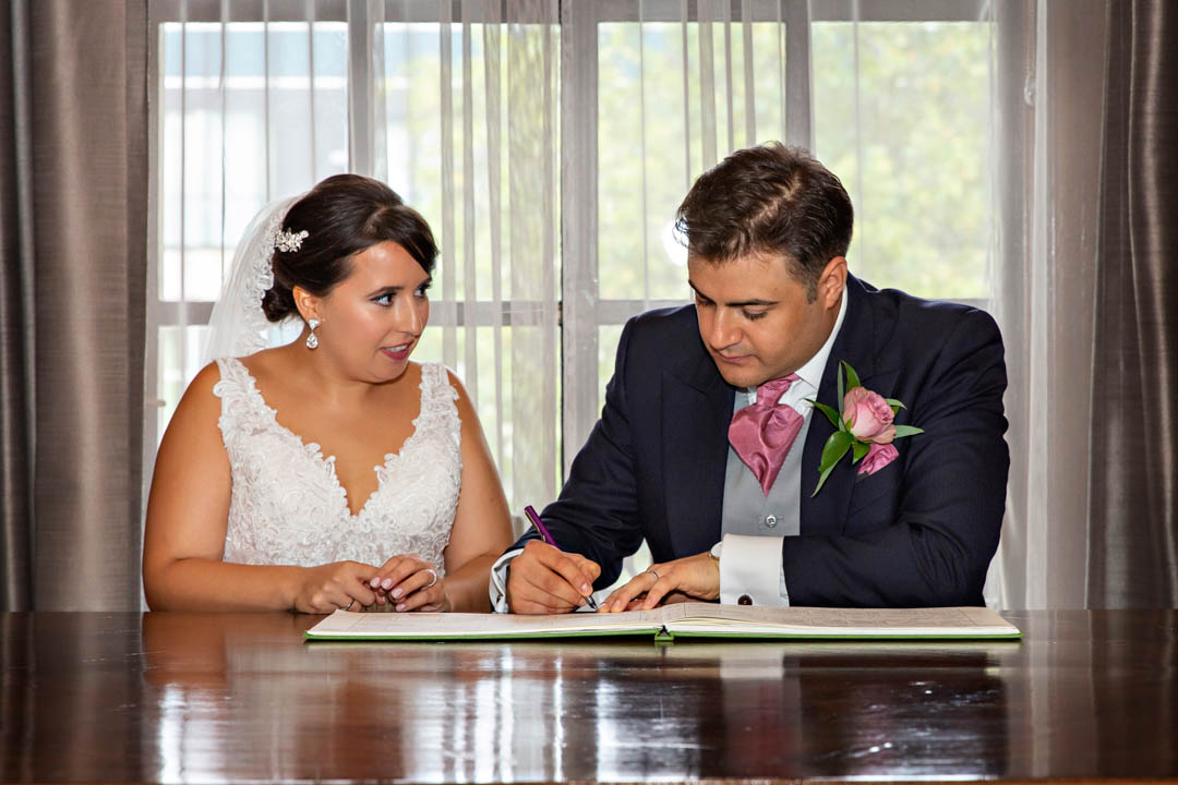 A bride looks on as the groom signs the wedding register in the Westminster Room.