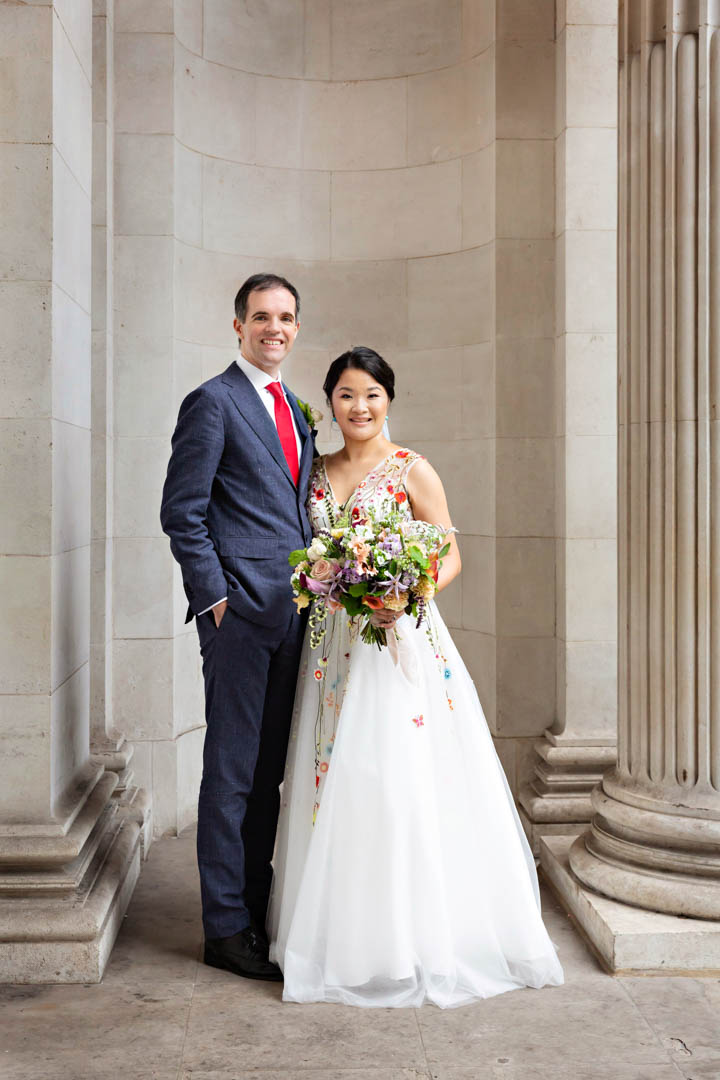 A classic timeless wedding portrait of a bride and groom after their Westminster Room wedding ceremony. The bride is holding a large bouquet and is wearing a full-length dress with full skirt and colourful decorative stitching.