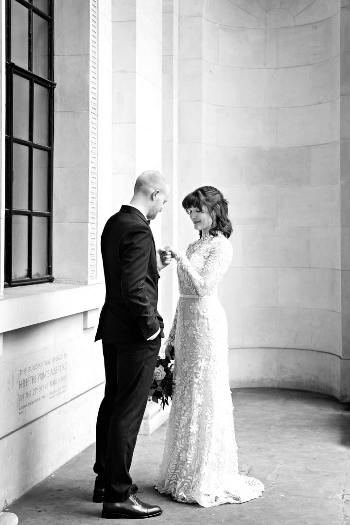 A black and white image of a quiet moment between a bride and groom, as the groom holds the bride's hand, admiring her wedding ring. The bride is wearing a stunning full length vintage lace wedding dress with full lace covered sleeve.
