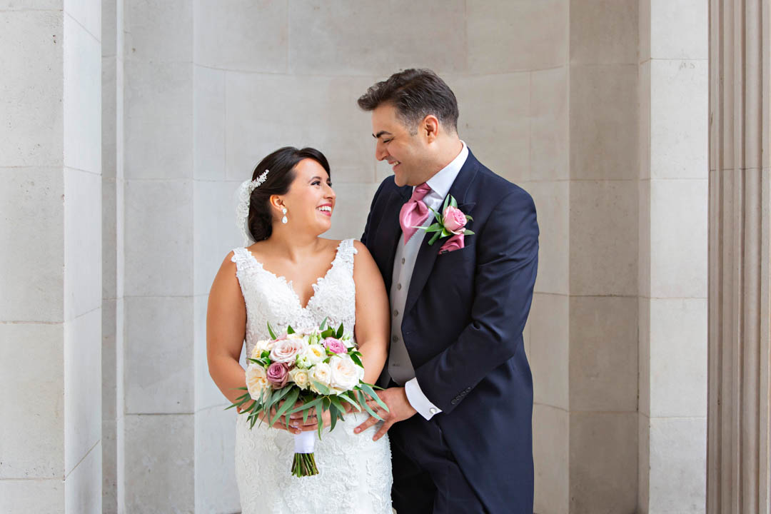 A bride and groom smile lovingly at each other during their wedding portrait photo session after their register office wedding in the Westminster Room.