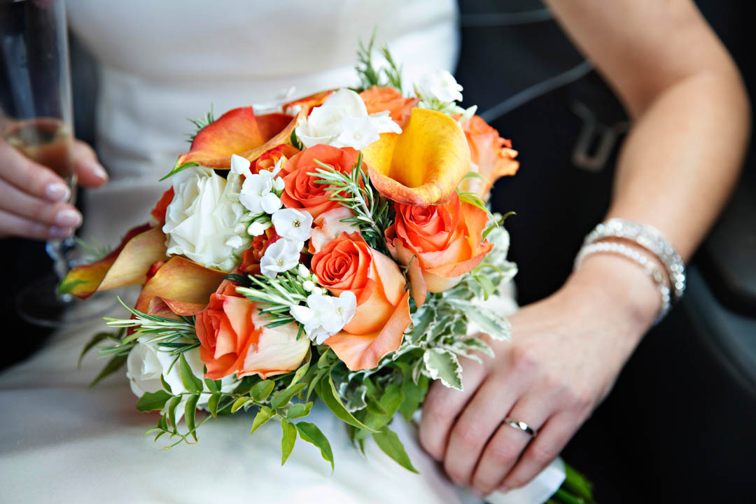 A closeup portrait of a stunning white and burnt orange bridal bouquet of orange calla lilies, and white and orange roses.